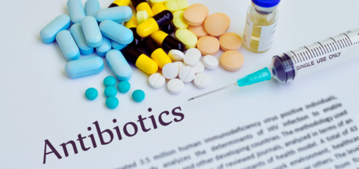 Różnorodne antybiotyki w postaci tabletek, kapsułek, fiolki z płynem i strzykawki na tle dokumentu z tytułem ‘Antibiotics’ – symboliczne przedstawienie tematu antybiotykoterapii i zagrożenia antybiotykoopornością.