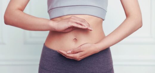 Zbliżenie na brzuch kobiety z dłońmi ułożonymi na podbrzuszu, ilustrujące temat zdrowia jelit, stanu zapalnego i metabolizmu.
