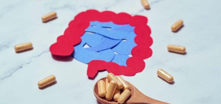 Ilustracja jelit otoczona kapsułkami probiotycznymi, symbolizująca temat mikrobioty oraz różnice między probiotykami, postbiotykami, synbiotykami, psychobiotykami i mykobiotykami.